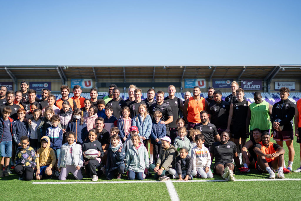 Joueurs de rugby posant avec des enfants sur le terrain.
